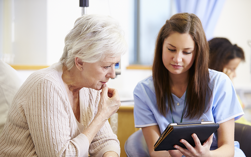 Woman and nurse sitting down and looking at an iPad.