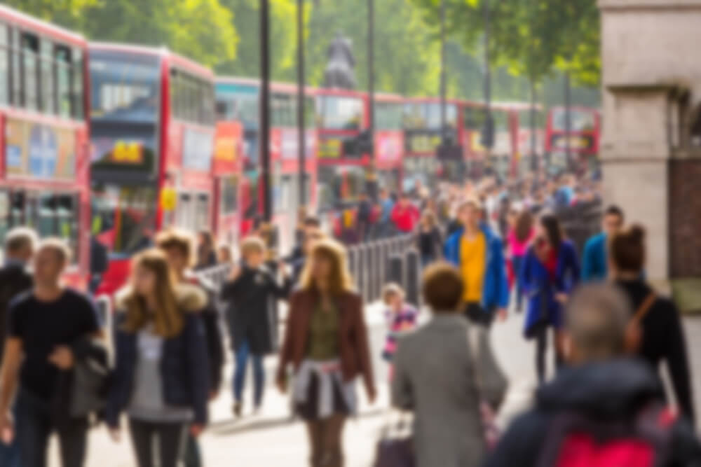 London streetscape with a row of red London buses to the left and crowds of people walking in both directions