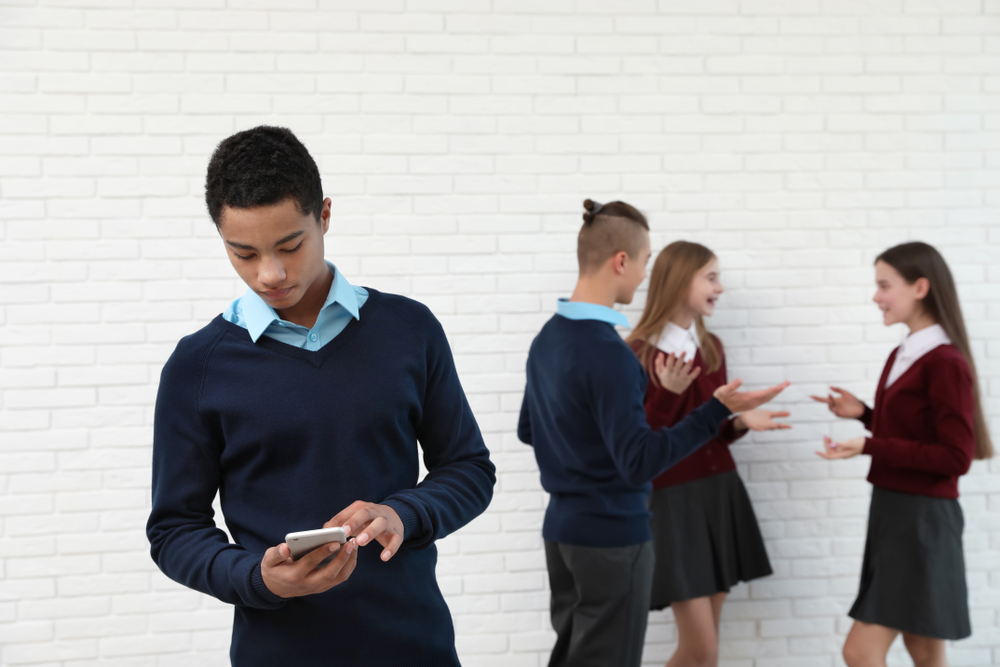 A teenage boy stands alone looking at his phone.