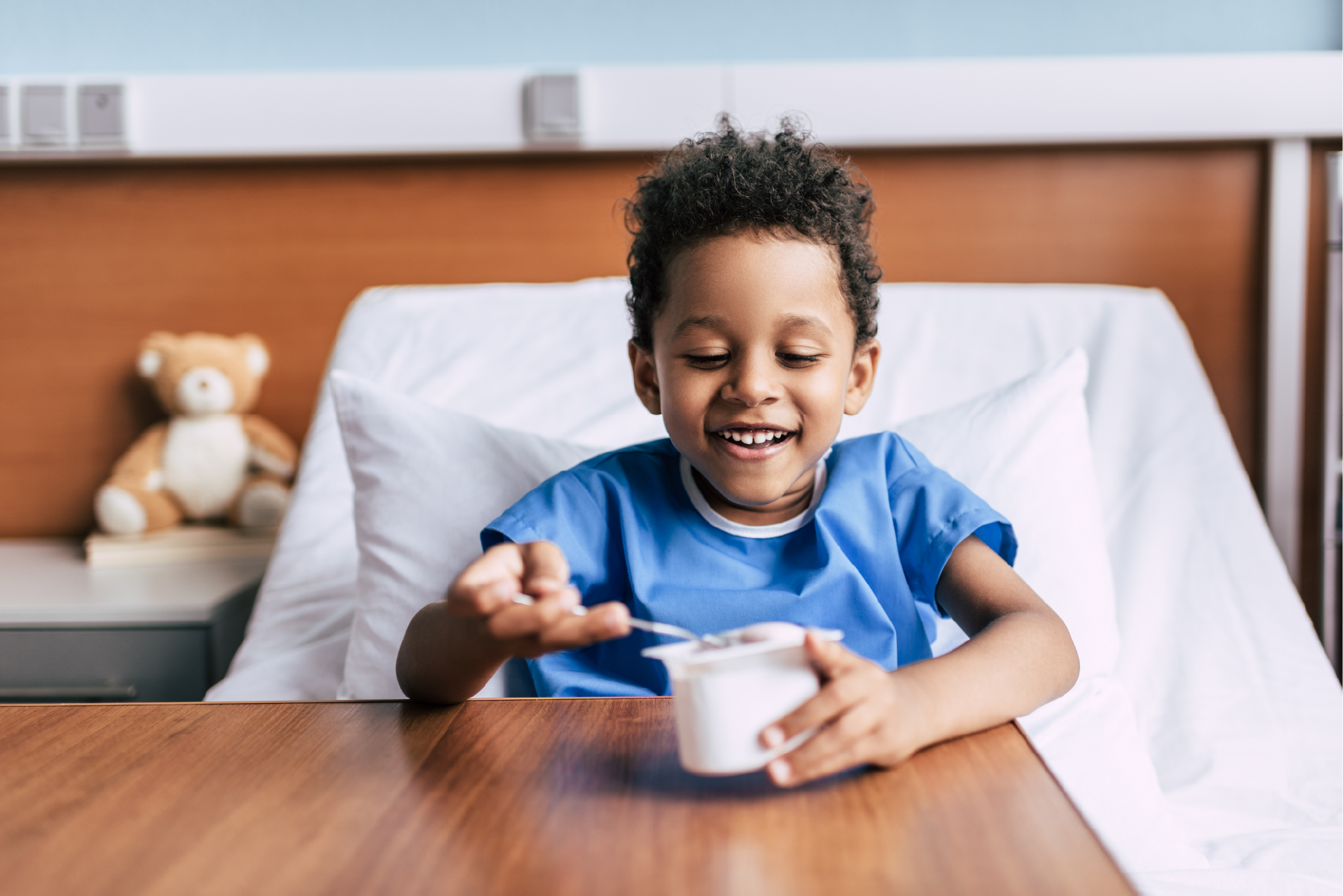 Child sat on a hospital bed eating from a pot