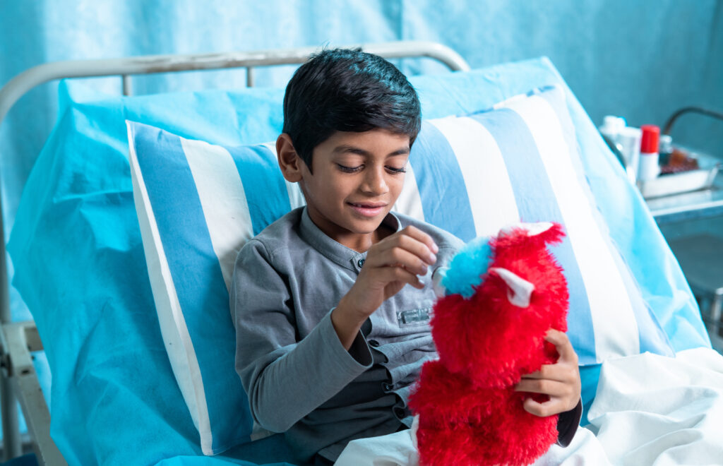 Happy sick child playing with teddy bear at hospital ward