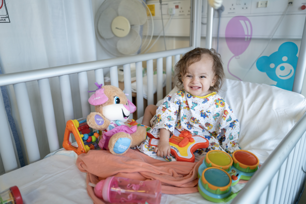 Smiling young child on hospital bed with toys