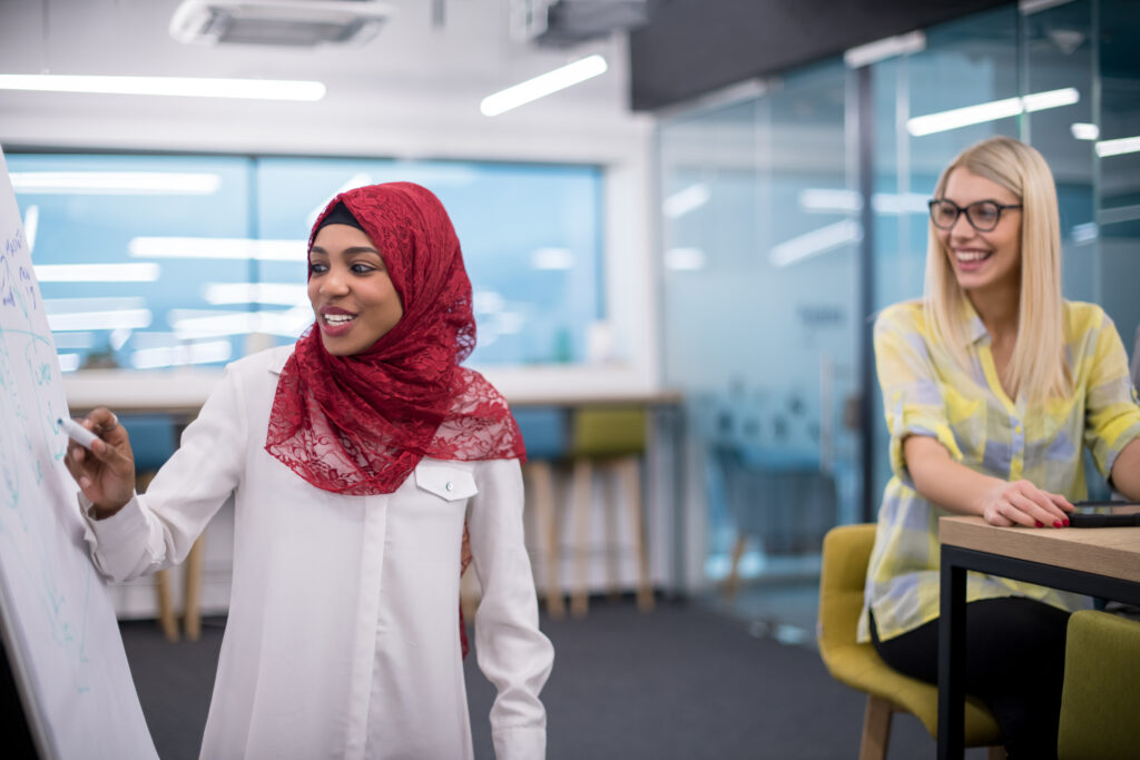 Smiling woman with red headscarf using a pen to write on a flipchart