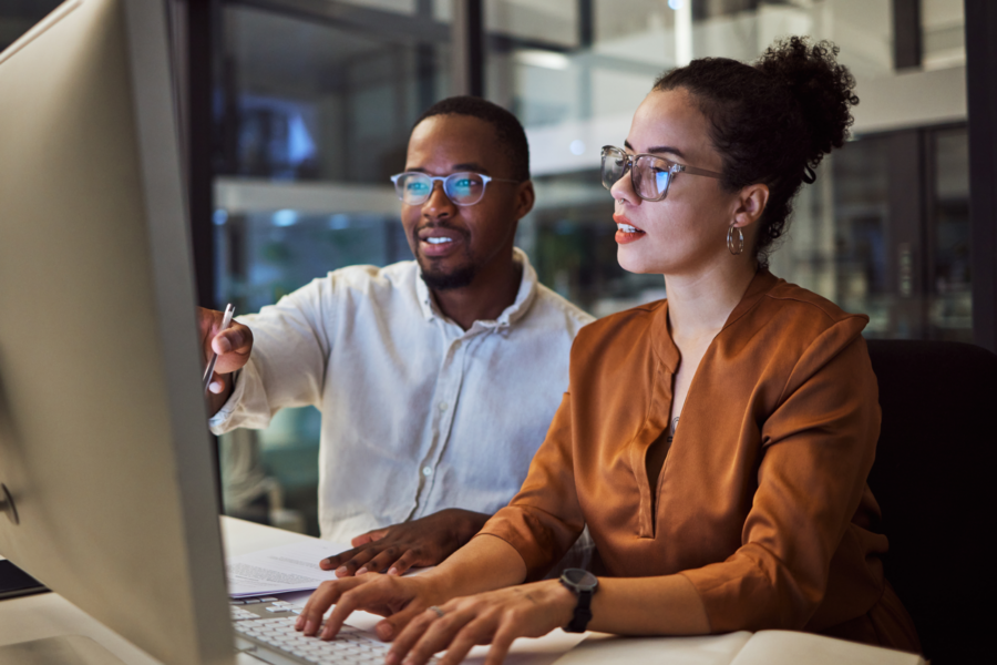 Two coworkers, one female presenting and one male presenting, looking at a computer
