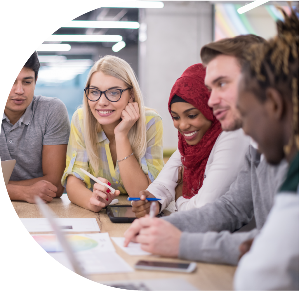 A group of male and female presenting people around a table smiling, one wearing a red head scarf