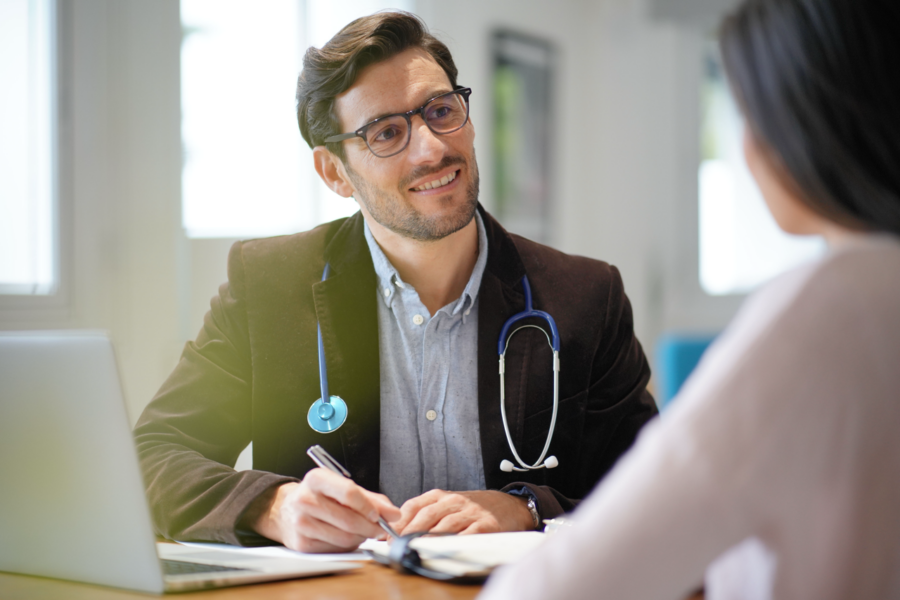 Male presenting doctor with stethoscope speaking to a female presenting person