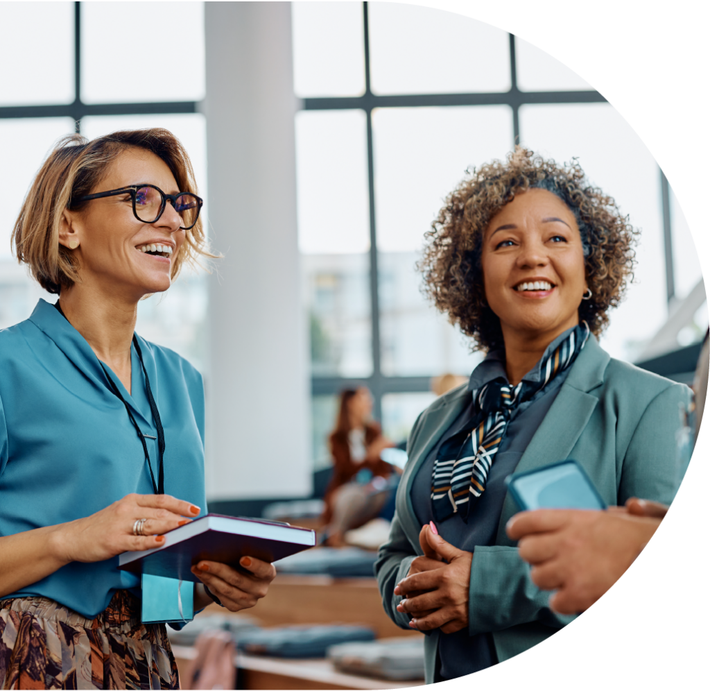 Two business women, one with a notepad, talking to a business man holding a mobile phone