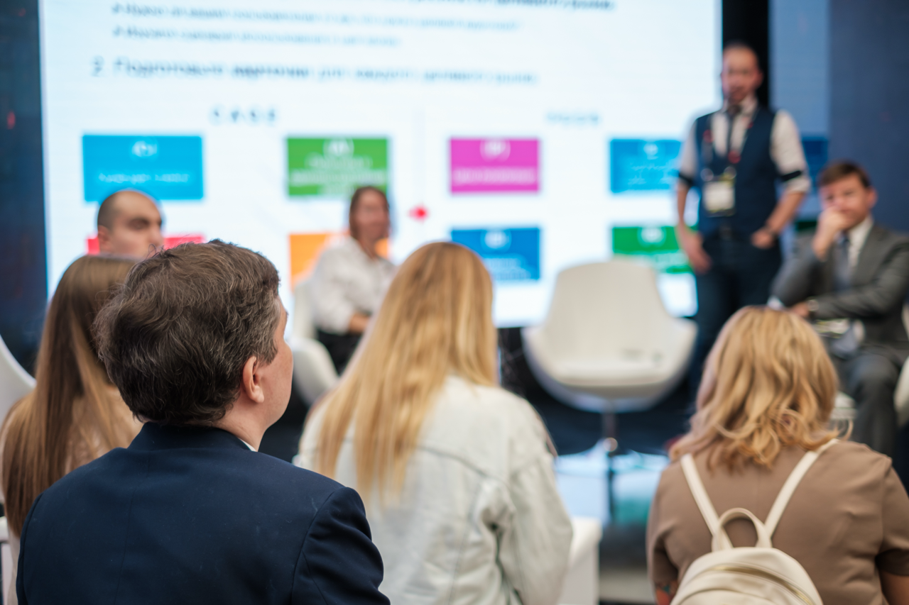 A group of attendees in a workshop, with a panel of speakers in front of a screen