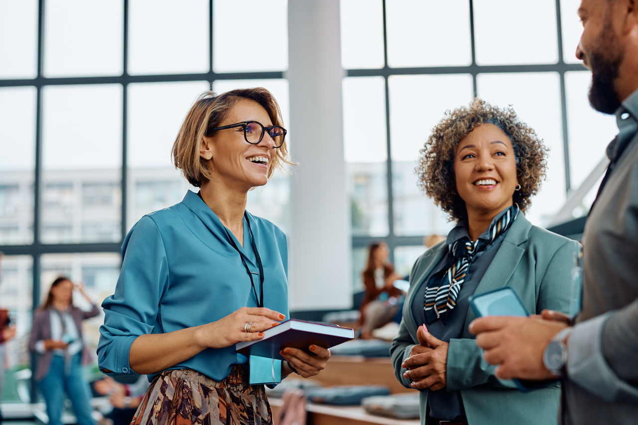 Two business women, one with a notepad, talking to a business man holding a mobile phone