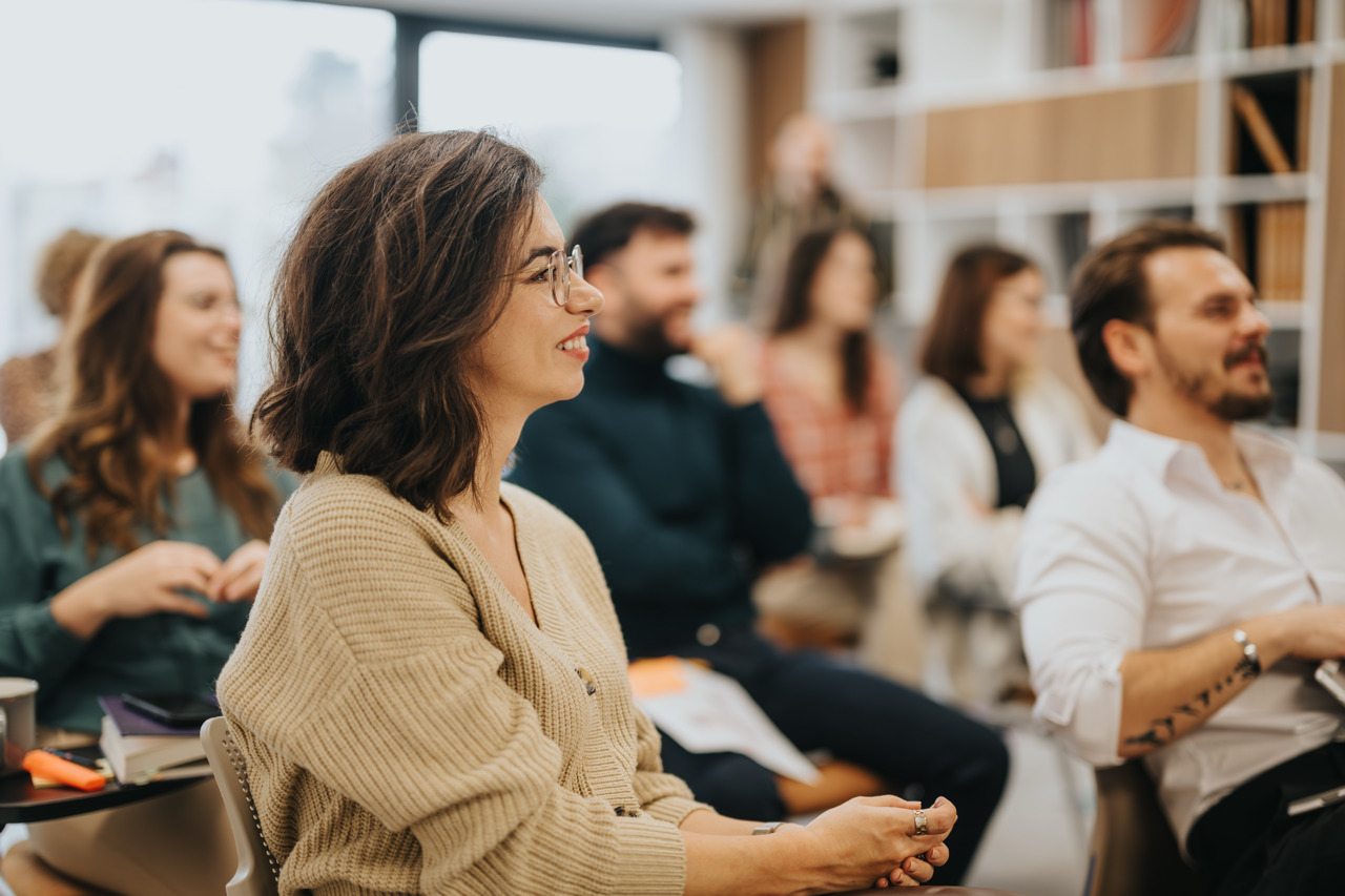 A group of people attending a training session, the camera focused on a female presenting person who is smiling