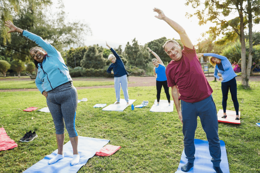 A group of people stretching in a park on mats