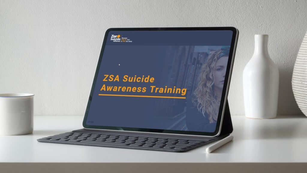 A tablet computer sits on a white desk, propped up by a keyboard case. The screen shows the title slide for the "ZSA Suicide Awareness Training," with the Zero Suicide Alliance logo in the corner and a photo of a woman looking thoughtfully to the side.