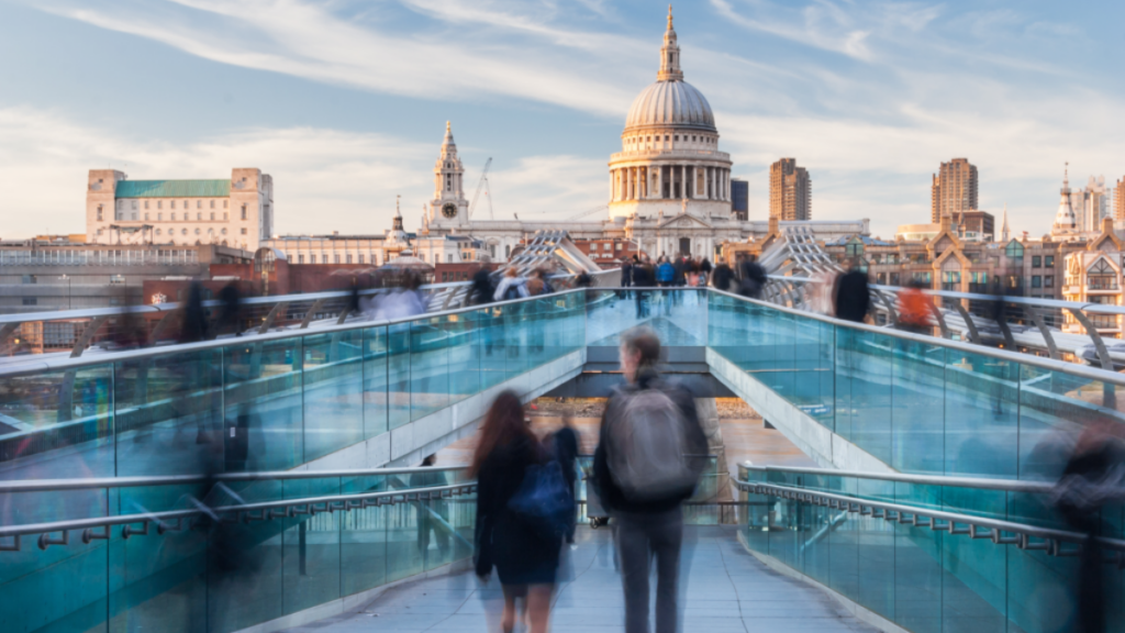 A wide view of people walking across London's Millennium Bridge towards St Paul's Cathedral on a bright day.