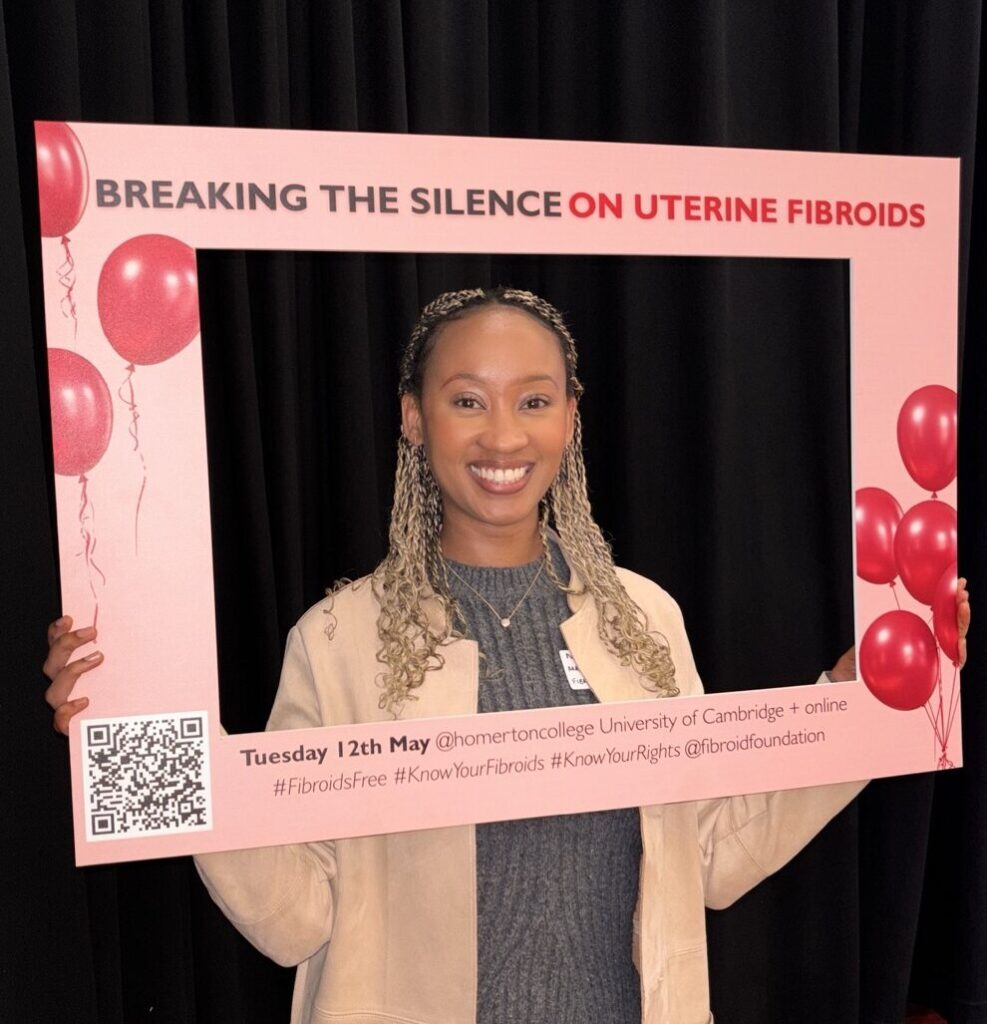 Natasha Wainaina holds a pink awareness frame reading ‘Breaking the Silence on Uterine Fibroids’ at an event promoting education and discussion about uterine fibroids.
