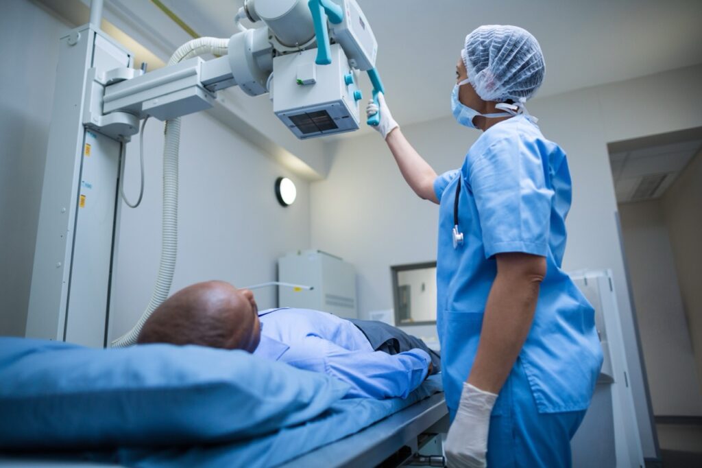 A healthcare professional positions an X-ray machine above a patient lying on an examination table in a radiography room.