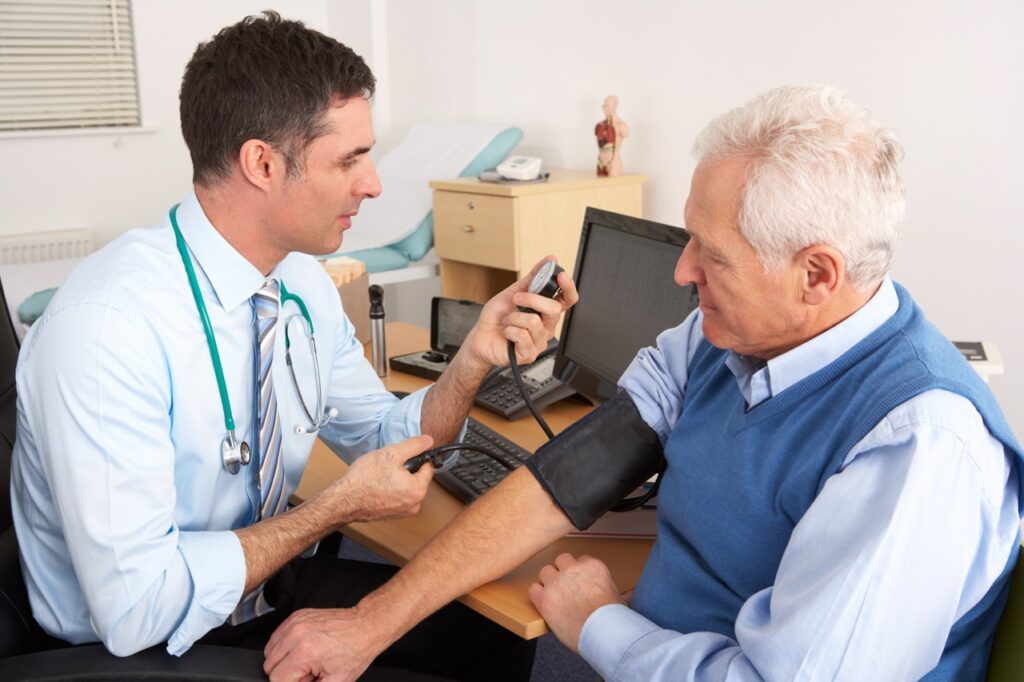 A healthcare professional checks an older man’s blood pressure during a consultation in a primary care setting.