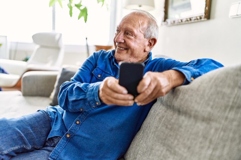 A man sitting on a sofa at home, holding a mobile phone.